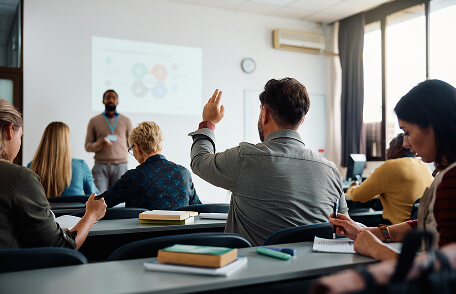 A man raising his hand in an adult group lecture setting