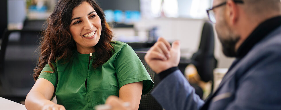 A woman talking and smiling at a man who is smiling and facing away from camera
